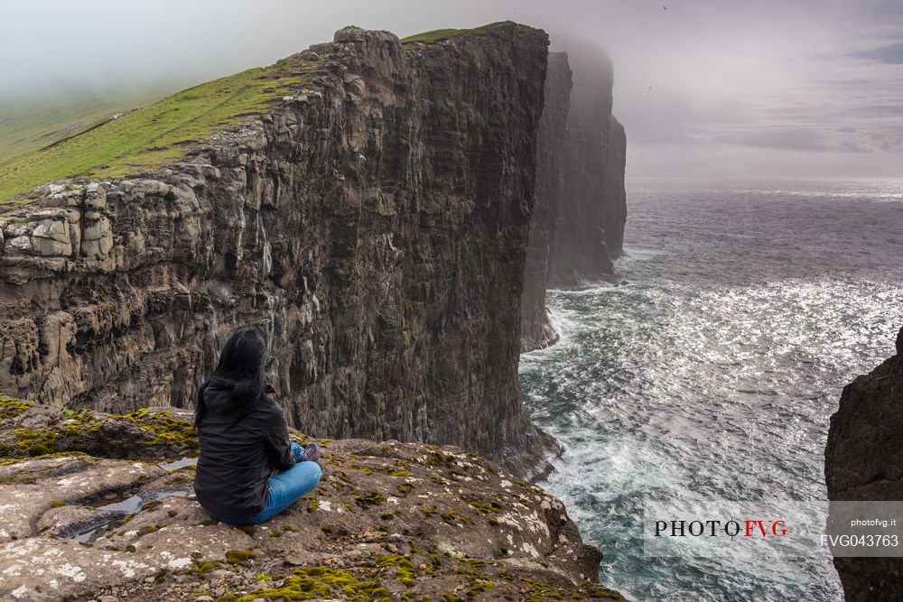 Tourist looking the stormy sea from the Srvgsvatn or  Leitisvatn cliffs, Faeroe Islands, Denmark, Europe