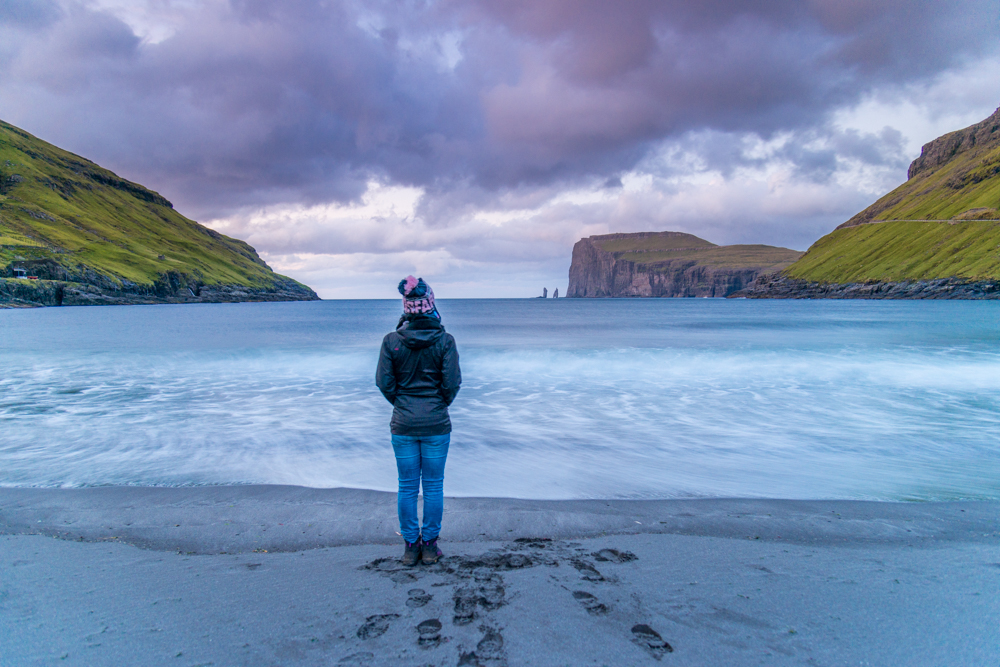 Tourist looking the wild sea and in the background the sea stacks of Risin and Kellingin, just off the northern coast of the island of Eysturoy from Tjornuvik village, Streymoy island, Faeroe islands, Denmark, Europe