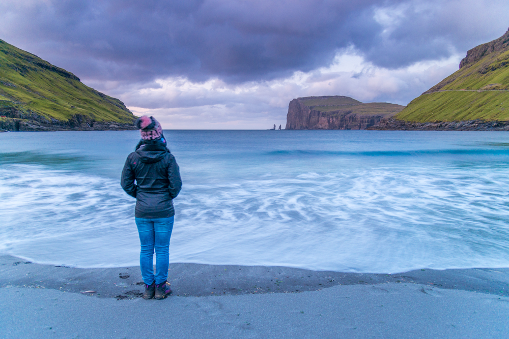 Tourist looking the wild sea and in the background the sea stacks of Risin and Kellingin, just off the northern coast of the island of Eysturoy from Tjornuvik village, Streymoy island, Faeroe islands, Denmark, Europe
