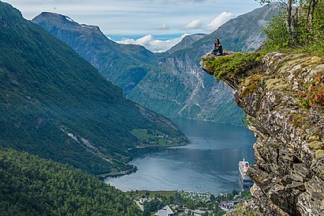 Girl relaxing on the Flydalsjuvet rock, over the Geiranger fjord, Norway