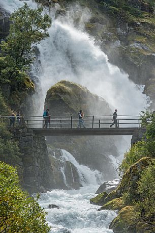 Tourist on the bridge of Briksdalsbreen waterfalls, popular touristic hike to Briksdal glacier, Norway