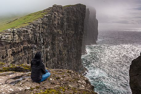 Tourist looking the stormy sea from the Srvgsvatn or  Leitisvatn cliffs, Faeroe Islands, Denmark, Europe