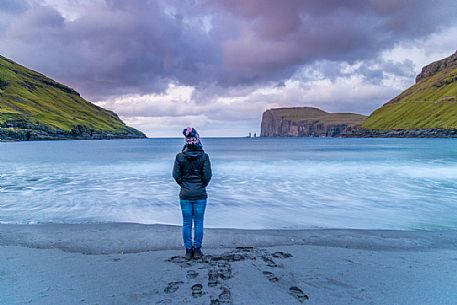 Tourist looking the wild sea and in the background the sea stacks of Risin and Kellingin, just off the northern coast of the island of Eysturoy from Tjornuvik village, Streymoy island, Faeroe islands, Denmark, Europe