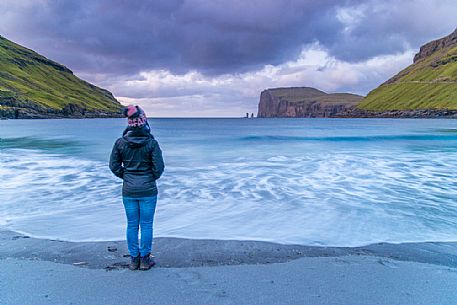 Tourist looking the wild sea and in the background the sea stacks of Risin and Kellingin, just off the northern coast of the island of Eysturoy from Tjornuvik village, Streymoy island, Faeroe islands, Denmark, Europe