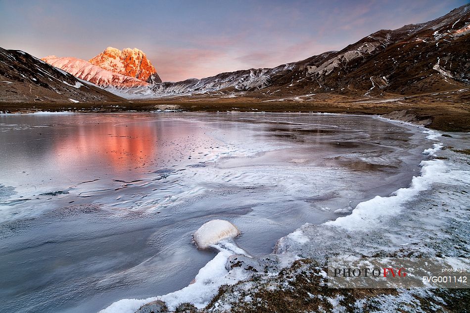 The Corno Grande peak reflected on the frozen Pietranzoni lake in a cold winter morning, Campo Imperatore, Gran Sasso and Monti della Laga national park