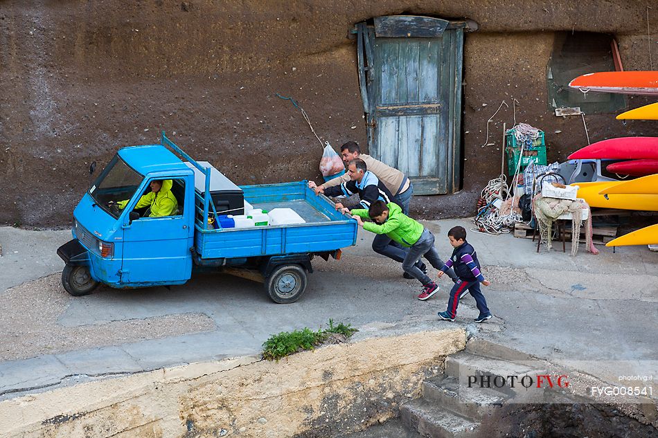 People pushing a Piaggio Ape Car in the roman harbor of Ventotene
