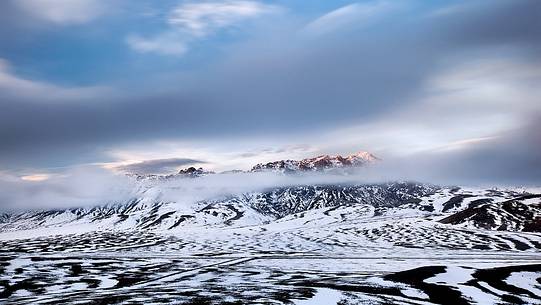 Clouds blown by the wind flow veiling the mountains lit by the last light of a winter sunset, Campo Imperatore, Gran Sasso e Monti della Laga National Park