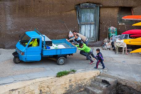 People pushing a Piaggio Ape Car in the roman harbor of Ventotene