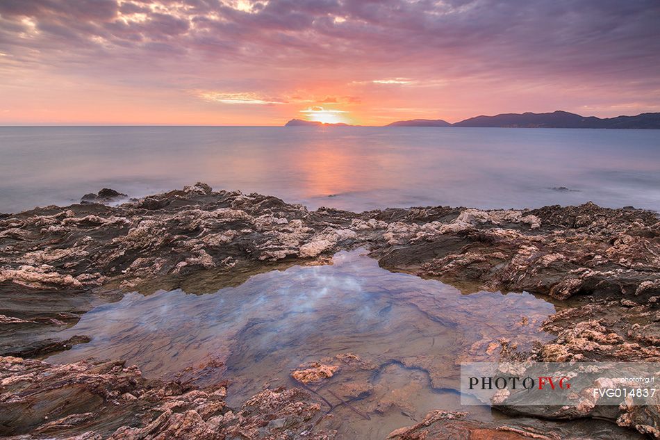 The colors of the rocks of the Piscinn bay appear lit from the sun on the horizon, giving unusual and attractive colors
