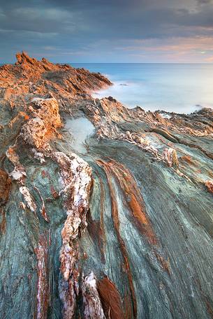 The colors of the rocks of the Piscinnì bay appear lit from the sun on the horizon, giving unusual and attractive colors, Sulcis-Iglesiente, Sardinia