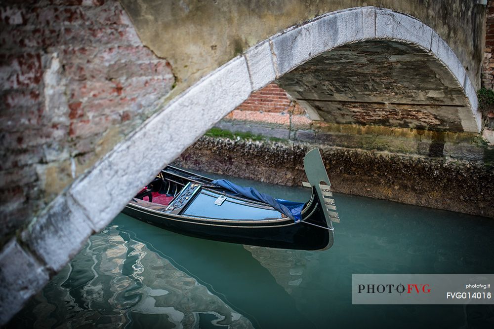 Detail of old gondola under the bridge on the canal in Venice, Veneto, Italy, Europe