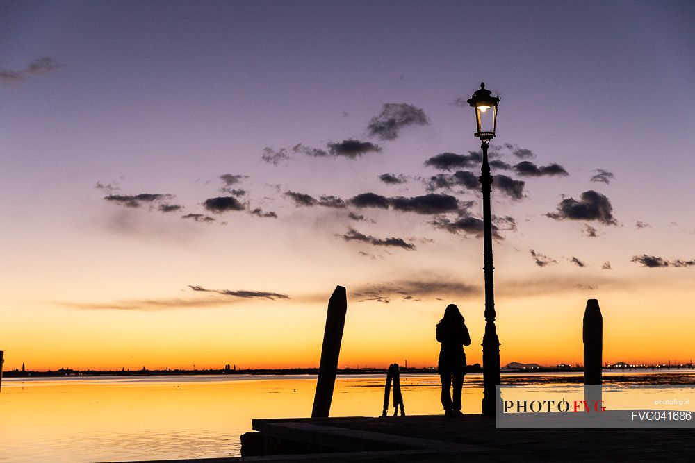 Woman in silhouette at twilight looking Venice island from Burano island, Venetian lagoon, Veneto, Italy, Europe