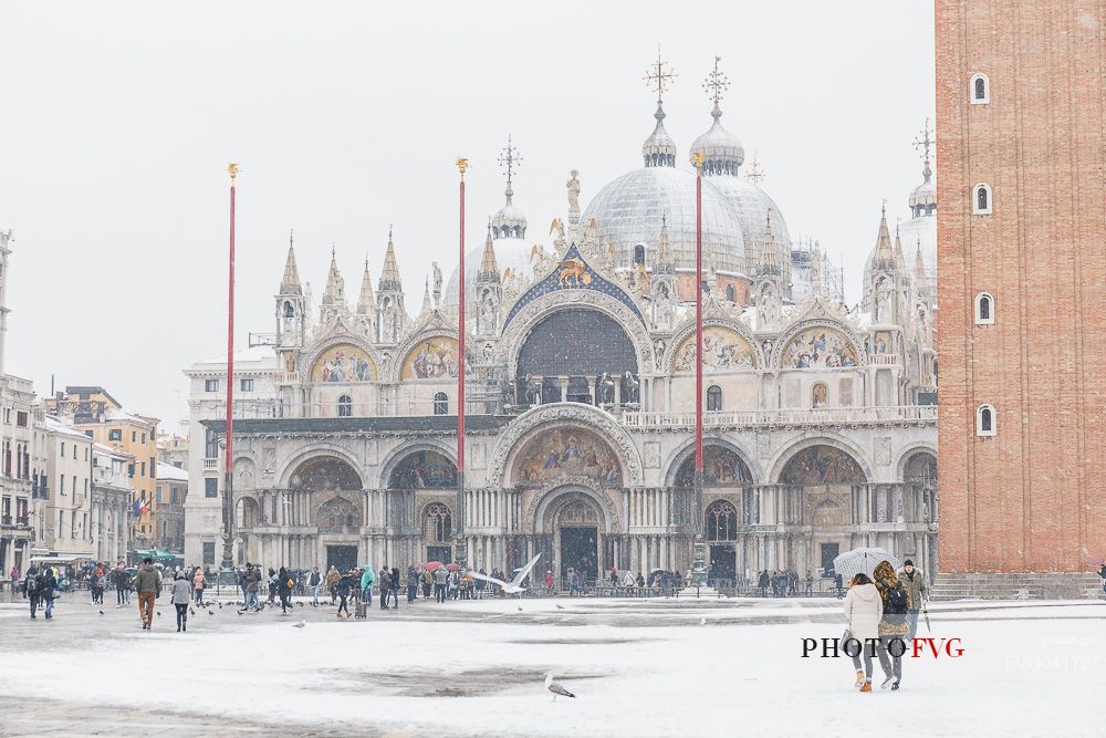 Tourists on Piazza San Marco or St Mark square and in the background the Basilica of San Marco church with bell tower in a snowy day, Venice, Italy