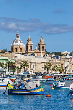 The historic city of Marsaxlokk on the island of Malta, famous for its colorful fishing boats called Iuzzu, in the background the Parish church dedicated to Our Lady of Pompeii, Malta, Europe