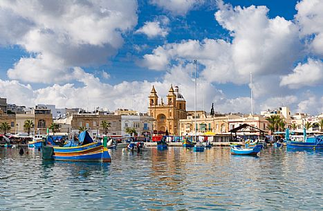 The historic city of Marsaxlokk on the island of Malta, famous for its colorful fishing boats called Iuzzu, in the background the Parish church dedicated to Our Lady of Pompeii, Malta, Europe