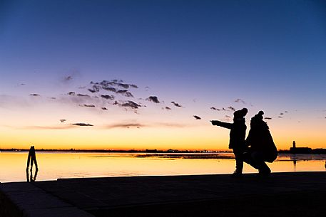 Silhouette of mother and child at twilight and in the background the island of Venice, from Burano island, Venetian lagoon, Veneto, Italy, Europe
