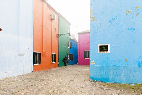 Back view of woman on walking in a typical alley of colored village fo Burano in a foggy day, Venice, Italyl, Europe