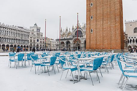 Snowy chairs on Piazza San Marco or St Mark square and in the background the Basilica of San Marco church with bell tower and the Doge Palace, Venice, Italy