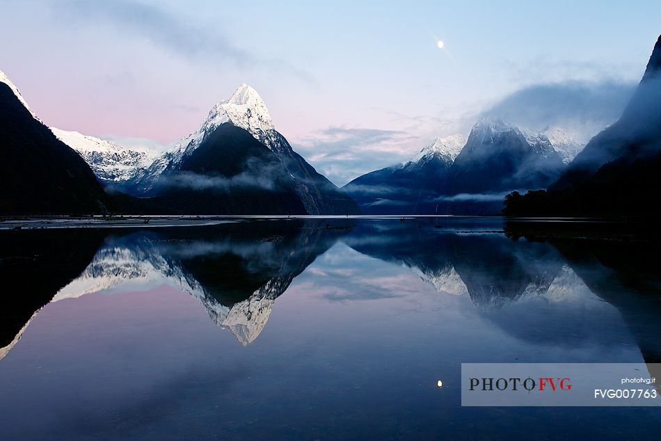 Moon and snow capped peaks reflected on the sound during an amazing sunrise in Fiorland Region.