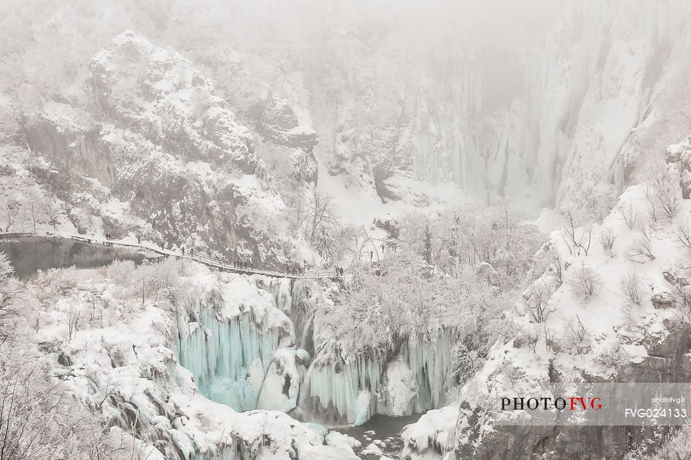 Tourists admiring frozen lakes and waterfalls in Plitvice Lakes National Park, Croatia