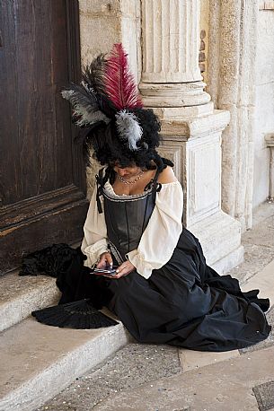 Woman with carnival dress rests under the loggia of Ducale Palace in Venice during teh carnival. Italy