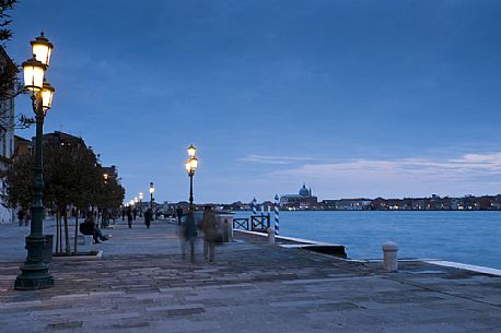 Tourists walk on the foundations of the Zattere in the Dorsoduro district of Venice. On the background the church of the Redentore or Redeemer on the Giudecca island, Italy.