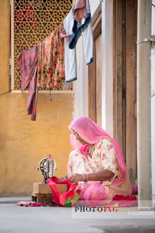 Indian woman sewing in front of her house door, Jaisalmer, Rajasthan, India