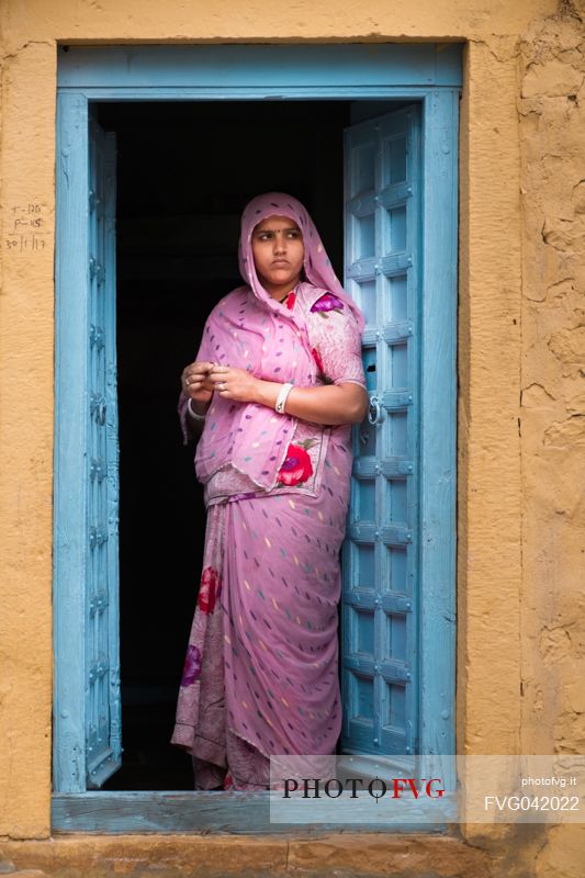 Young indian Rajasthani woman dressed in sari standing on the threshold of her house, Rajasthan, India
