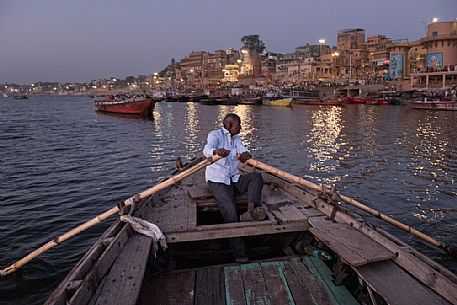 Man rowing in his little boat along the river Ganges in Varanasi during sunrise, the city in the background, Uttar Pradesh