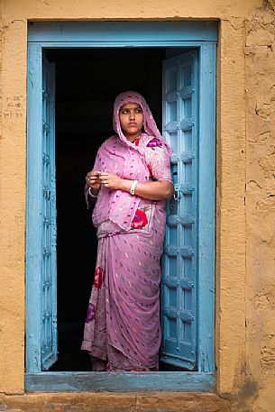 Young indian Rajasthani woman dressed in sari standing on the threshold of her house, Rajasthan, India