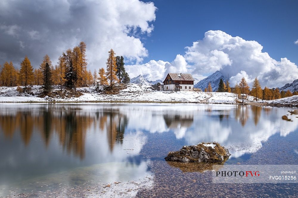 The Palmieri refuge and the orange larches reflected on the clear water of Federa lake 