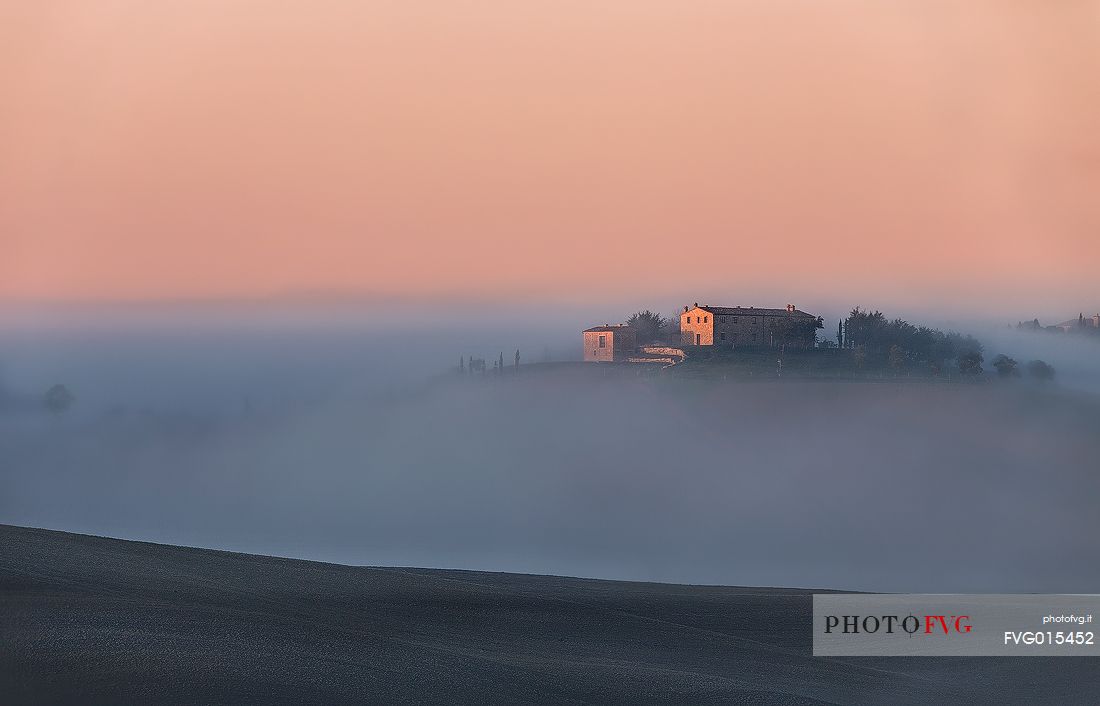 the fog of an autumn sunrise cover the homes of the Val D'Orcia