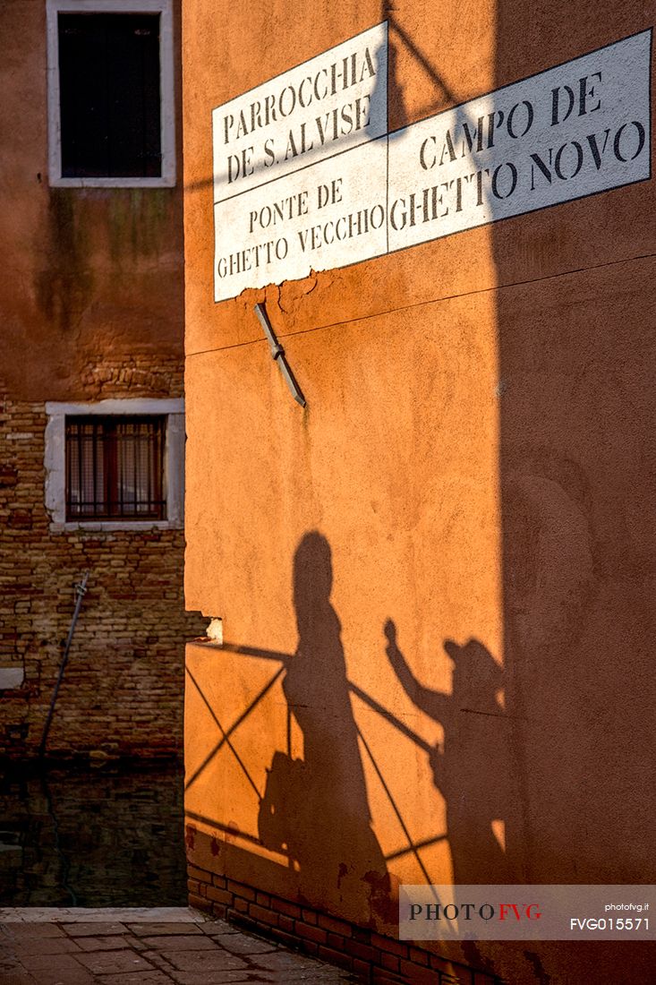 Shadows of two tourists while taking a photo on the bridge of Ghetto Vecchio in Venice