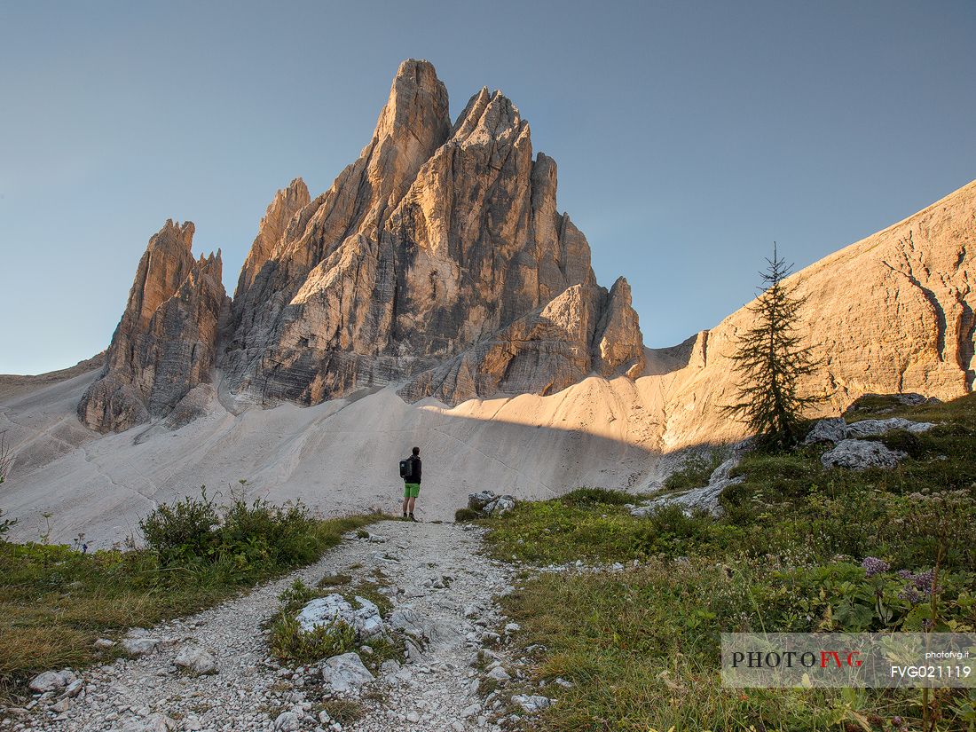 Hiker near the alpine hut of Zsigmondy - Comici with the Croda dei Toni on background lit by sunset, Sexten dolomites, Tre Cime natural park, Dolomites, South Tyrol, Italy, Europe