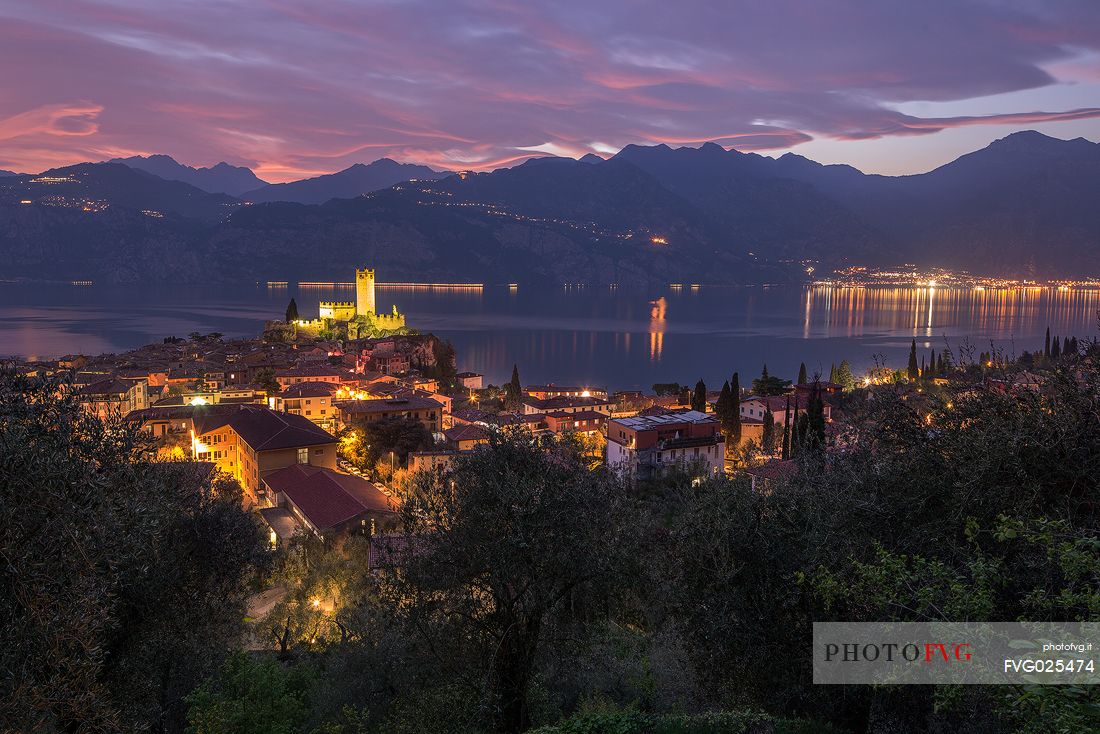 Panoramic view of the small medieval village of Malcesine with the castle Scaligero overlooking Garda lake shortly after a fiery sunset, Italy