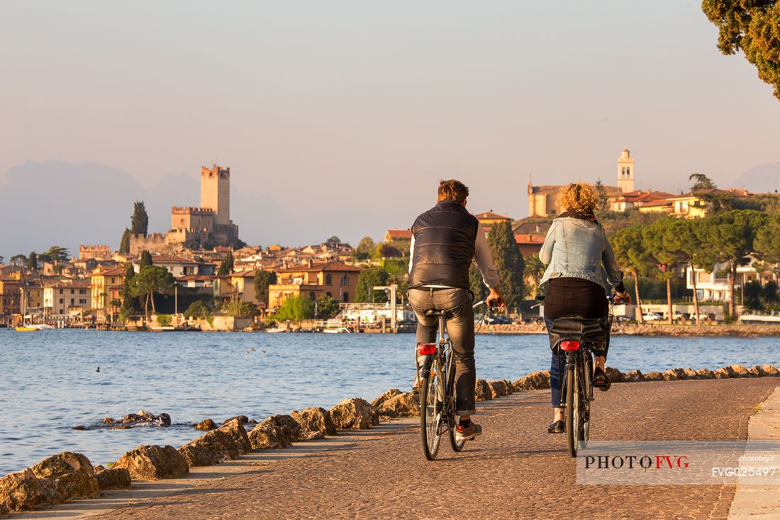 Bicycle couple along Garda lake, in the background the small medieval village of Malcesine, Italy