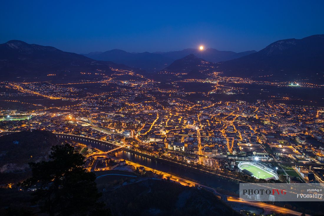 The moon arises behind the mountains over the Trento city photographed by Sardagna hamlet, Trento, Trentino Alto Adige, Italy