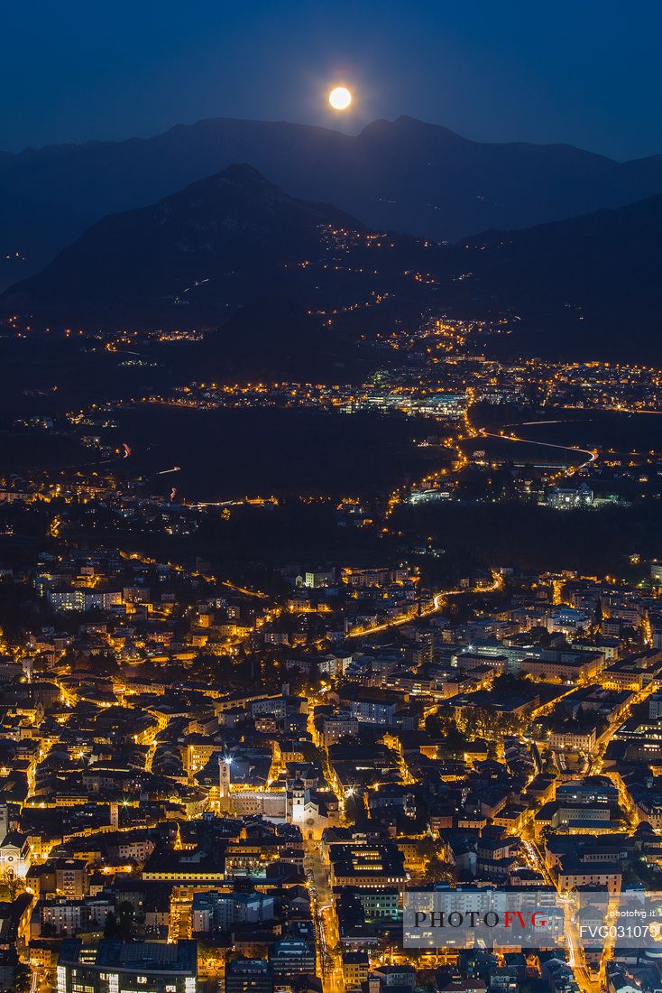 The moon arises behind the mountains over the Trento city photographed by Sardagna hamlet, Trento, Trentino Alto Adige, Italy