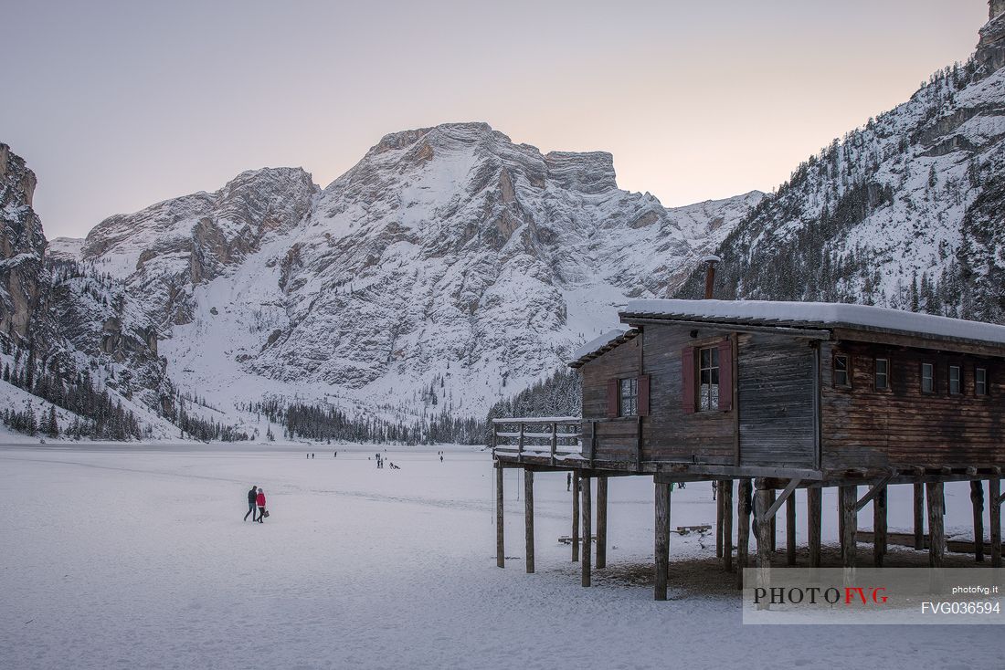 Tourists walk on the frozen Braies lake, on background the Croda del Becco mount, Braies, Pusteria valley, Trentino Alto Adige, Italy, Europe