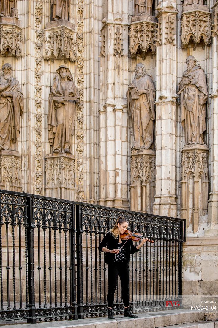 A street artist plays the violin under the facade of the Cathedral of Seville or Church of Santa Maria della Sede, Seville, Spain, Europe