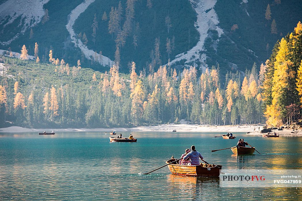 Tourists on boat in the Braies lake with autumn colors, dolomites, Pusteria valley, Trentino Alto Adige, South Tyrol, Italy, Europe