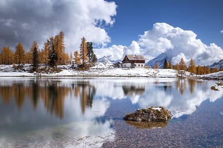 The Palmieri refuge and the orange larches reflected on the clear water of Federa lake 