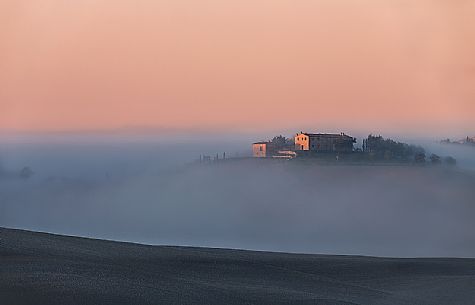 the fog of an autumn sunrise cover the homes of the Val D'Orcia
