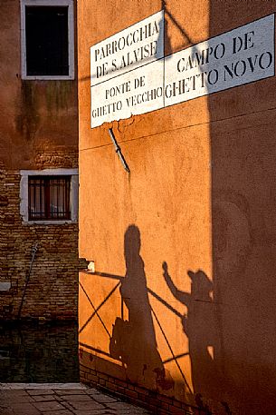 Shadows of two tourists while taking a photo on the bridge of Ghetto Vecchio in Venice