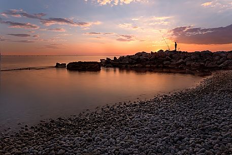 Fisherman at sunset on the beach rocks of ''Canovella degli Zoppoli ' ' in Trieste