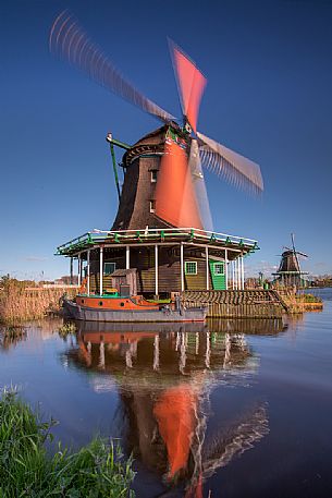 The wind moves the blades of the mill on the banks of the river Zaan in the little village of Zaanse Schans