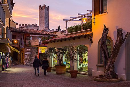 Evening walk in the alleys of the medieval village of Malcesine, in the background the castle of Scaligero, Garda lake, Italy