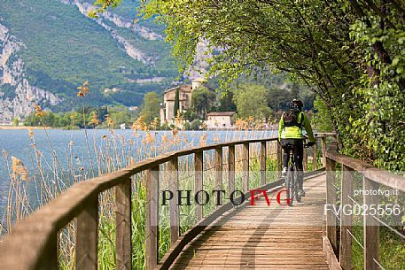 Cyclist along the catwalk of the Toblino lake, on background the Toblino castle, Valley of Lakes, Italy 