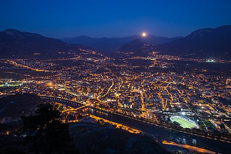 The moon arises behind the mountains over the Trento city photographed by Sardagna hamlet, Trento, Trentino Alto Adige, Italy