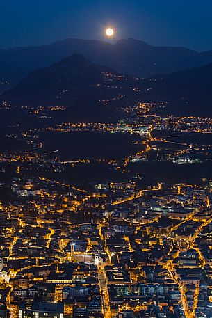 The moon arises behind the mountains over the Trento city photographed by Sardagna hamlet, Trento, Trentino Alto Adige, Italy